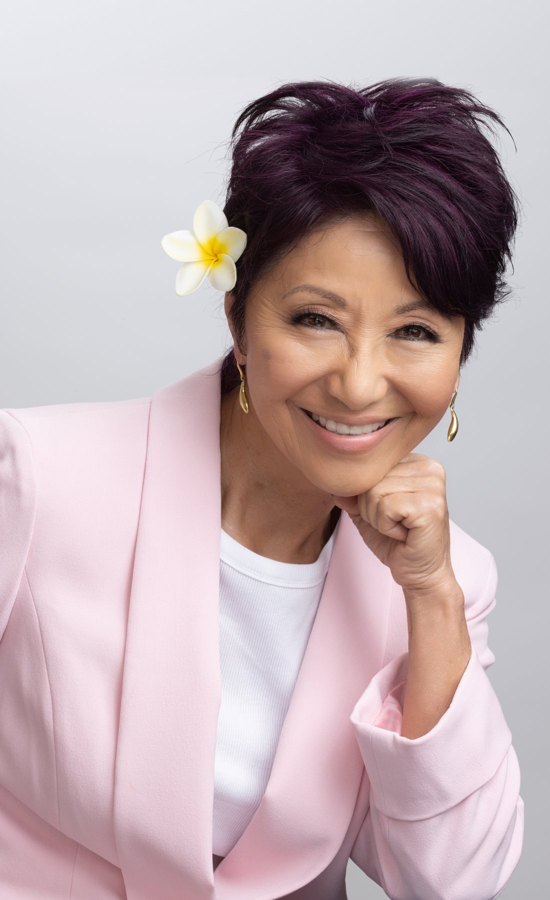 Olelo paʻa Ogawa smiling in a pink blazer with a plumeria flower in her hair