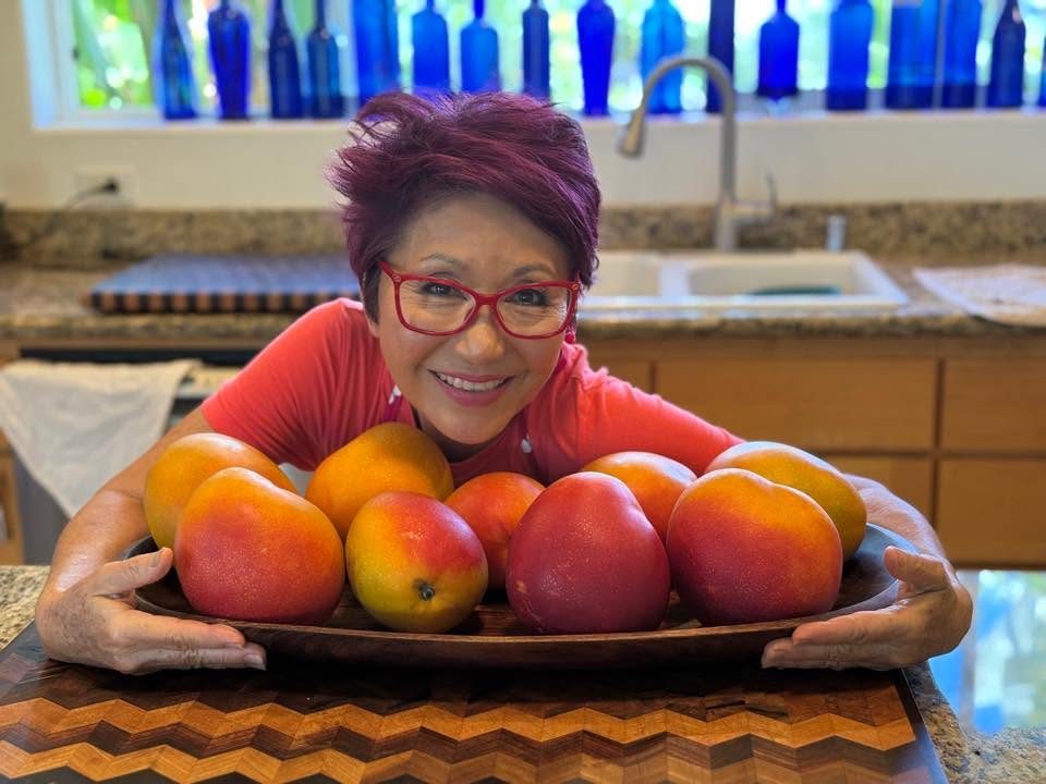 Olelo paʻa smiling behind a bowl of fresh mangoes in her kitchen